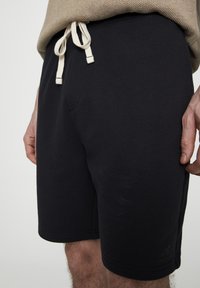 Shorts en coton noirs avec une taille élastique et un cordon de serrage, une poche latérale et un petit logo en bas à gauche.
