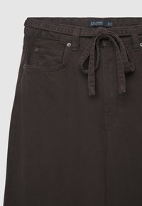 Dunkelbraune Jeanshose mit gebundenem Bund, zwei Vordertaschen und dezenten Nähten; glatte Textur und lockerer Schnitt.
