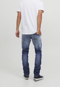 Dżinsy z denimu w ciemnym niebieskim kolorze z jasnym przetarciem, o dopasowanym kroju i detalem przeszyć na tylnych kieszeniach. Połączone z prostą białą koszulką i tenisówkami.