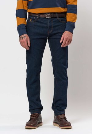 Mann trägt dunkelblaue Jeans, braunen Ledergürtel, gestreiftes orange-blaues Langarmshirt und braune Leder-Schnürstiefel.