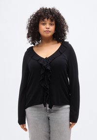 Blouse noire à manches longues avec col à volants et fermeture devant. Tissu doux, coupe décontractée, col en V et détail élégant à volants.