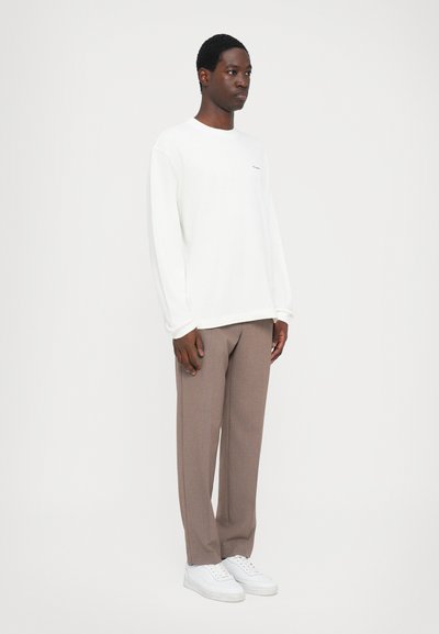 White long-sleeve shirt with a round neckline, paired with light brown tailored trousers and white sneakers. Simple design, minimalistic details.