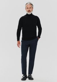 Czarny sweter z golfem, dopasowane granatowe spodnie i wypolerowane czarne buty. Gładkie faktury i elegancki wygląd bez widocznych wzorów.