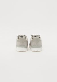 Baskets de sport gris clair avec une tige en tissu texturé, un talon renforcé et une semelle en caoutchouc blanche. Présente une marque à l'arrière.