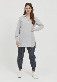Camicia tunica leggera a righe bianca e blu navy, con colletto e maniche lunghe, abbinata a pantaloni jogger a righe blu navy, con polsini elasticizzati.
