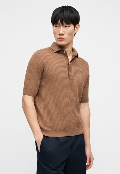 Καφέ κοντομάνικη πόλο μπλούζα με ριμπ υφή, με γιακά και δύο κουμπιά. Συνδυάζεται με σκούρο παντελόνι και έχει εφαρμοστή σχεδίαση.