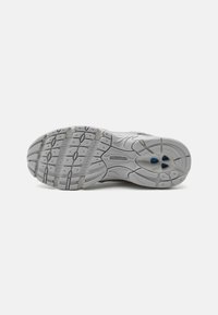 Suela de zapato deportivo gris con goma texturizada, patrón de tracción multidireccional y tres puntos de acento azules. Soporta el agarre y la estabilidad.