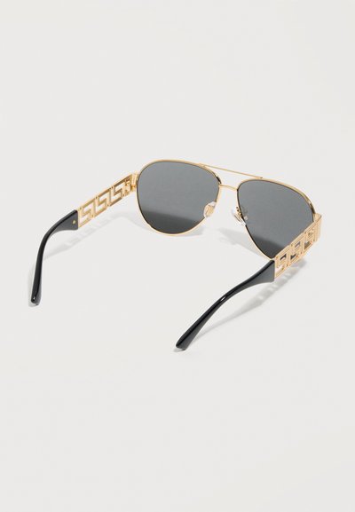 Goudkleurige aviator-zonnebril met donkere glazen en zwarte pootjes, met een geometrisch uitgesneden patroon op de armen.