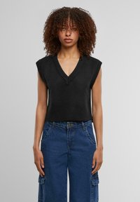 Top in maglia nera senza maniche con scollatura a V e orlo a coste, abbinato a pantaloni cargo blu in denim a vita alta e larghi, dotati di tasche laterali.