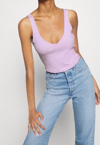 Débardeur côtelé lilas avec un décolleté en V profond, associé à un jean taille haute en denim clair. Présente une silhouette ajustée et des coutures minimales.