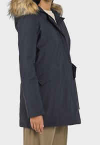 Námornícky modrá nepromokavá parka s kapucí s umělou kožešinou, bočními kapsami a rovnými liniemi, se hladkým povrchem a zajištěním.