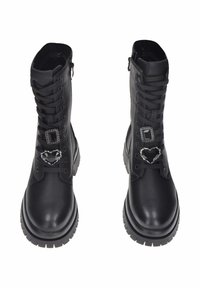 Un paio di stivali da combattimento in pelle nera con suole spesse, lacci, cerniere laterali e charm decorativi a forma di cuore e quadrato neri, simili a gemme, sui lacci.