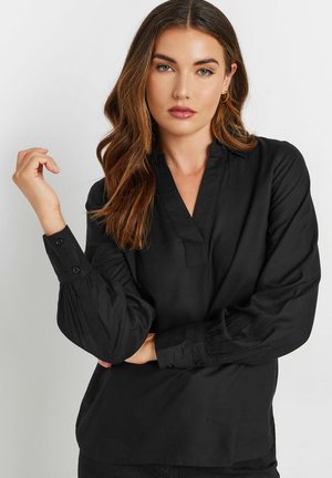 Blouse noire en tissu lisse avec un col en V, des poignets boutonnés et des manches froncées. Présente une coupe confortable et un design minimaliste.