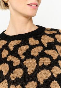 Strickpullover mit einem schwarzem und beigem Leopardenmuster, Rundhalsausschnitt und texturierter Oberfläche. Der Stoff wirkt weich und warm.