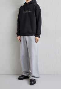 Sudadera negra con letras impresas, combinada con pantalones de chándal grises. Calzado negro con un diseño texturizado. Atuendo minimalista y casual.