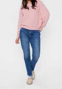 Ljusrosa stickad tröja med avslappnad passform, kombinerad med blå jeans med normal midja och beiga loafers. Har en mysig textur och en ledig design.