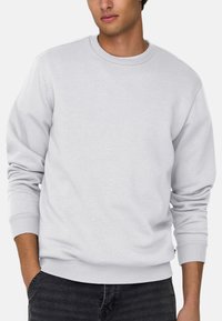 Witte crewneck sweatshirt gemaakt van een katoenmix, met ribbels aan de mouwen en onderkant, gedragen met donkere jeans. Gladde textuur en eenvoudig ontwerp.