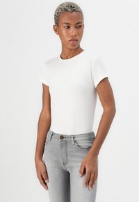 Hvit ribbet t-skjorte med kort erme og en tettsittende design, paret med lysegrå slim-fit jeans med metal knapp og frontlommer.