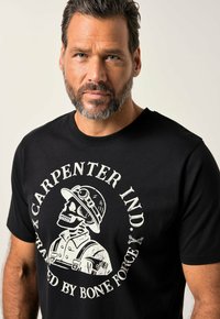 Camiseta de algodón negra con gráfico de calavera vintage en blanco, que lleva un casco de minero, acentuado por "CARPENTER IND." y "TRAINED BY BONE FORCE."