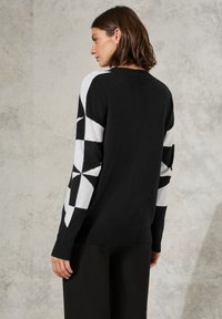 Maglione a fantasia bianca e nera con design geometrici, maniche lunghe, polsini a coste e collo rotondo. Tessuto morbido e vestibilità comoda.
