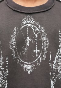 Μαύρο βαμβακερό t-shirt με σκισμένη στρογγυλή λαιμόκοψη και λευκό γραφικό σχέδιο ενός πλαισίου με σταυρούς και περίτεχνες λεπτομέρειες.