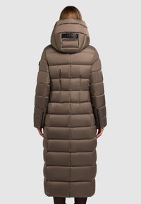 Rudas paminkštas ilgas paltas su kapišonu, vertikaliai ir horizontaliai siuvinėti skyreliai, su logotipo pleistru ant nugaros, turi ilgas rankoves.