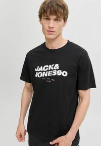 Sort bomulds T-shirt med fed, hvid distressed tekst "JACK & JONES" på forsiden. Klassisk crew neck med korte ærmer.