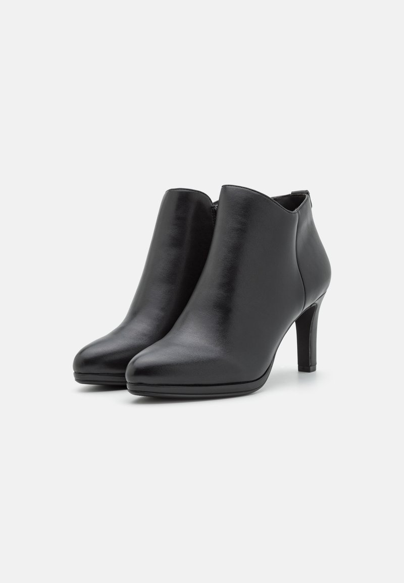 Bottines en cuir noir avec des orteils arrondis et des talons de hauteur moyenne, présentées sur un fond blanc uni.