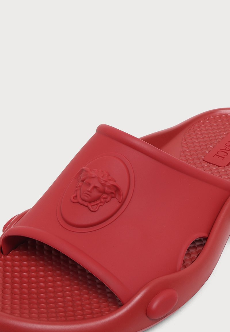 Rote Slides-Sandale mit strukturierter Innensohle und erhabenem Medusa-Kopf-Emblem auf dem Riemen.