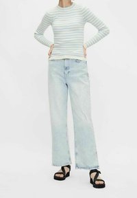 Pruhovaný dlouhý rukáv v světle modré a krémové barvě; volné světle prané džíny; černé platformové sandály s kříženými popruhy. Jednoduché pozadí.