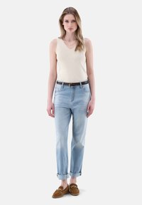 Beige gerippter Tank-Top kombiniert mit hellblauen hochgekrempelten Jeans. Ein brauner Ledergürtel und braune Slipper runden das Outfit ab.