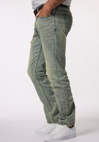 Vaqueros de mezclilla verde claro con corte ajustado, que presentan bolsillos frontales y un ligero desvanecimiento. Combinados con zapatillas blancas para crear contraste.