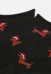 Černé ponožky s žebrovanou texturní, zdobené opakujícím se vzorem hnědých jezevčíků v červených vánočních čepicích a šálách.