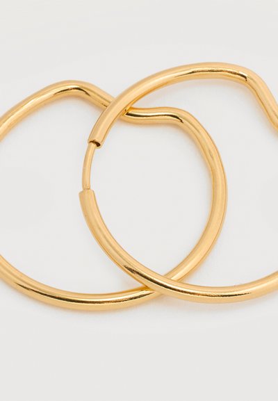 Δύο λεία, ακανόνιστου σχήματος χρυσά κρίκοι σκουλαρικιών με κούμπωμα, σε ανοιχτό φόντο.