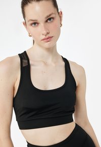 Schwarzer Sport-BH mit Rundhalsausschnitt, Netzakzenten an den Schultern und einer figurbetonten Silhouette. Glattes Material und dehnbare Textur.