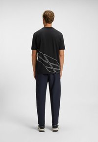 Sort t-shirt med hvide grafiske linjer på ryggen, kortærmet og med rund halsudskæring, parret med marineblå bukser og sorte sneakers.