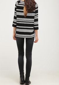 Černobíle pruhovaný top s designem do V na zádech, tříčtvrteční rukávy, spárovaný s černými skinny džíny a kotníkovými botami.