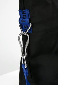 Borsa in tessuto nero con tracolla blu con testo, moschettone argentato e superficie testurizzata, progettata per durata e funzionalità.