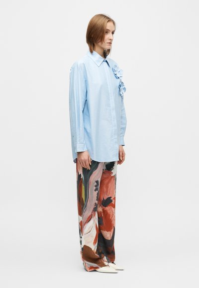 Cămașă bleu deschis cu nasturi și guler, decorată cu accente florale tridimensionale pe pieptul stâng, asortată cu pantaloni largi cu model.