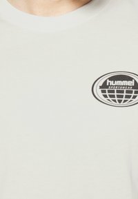 Světle šedé bavlněné tričko s kulatým výstřihem a krátkým rukávem, s černým oválným logem s nápisy "hummel" a "sportswear".