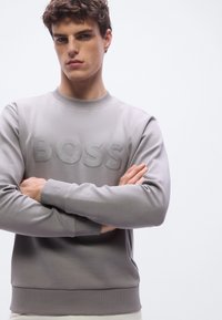 Γκρι φούτερ με στρογγυλή λαιμόκοψη, με ανάγλυφο λογότυπο «BOSS» στο μπροστινό μέρος και ριμπ μανσέτες και τελείωμα. Ομαλό υλικό με ματ φινίρισμα.