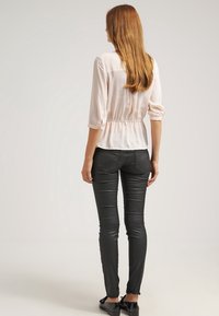 Jasnoróżowa bluzka z rękawami trzyczwartowymi, zebranym w pasie, o gładkiej fakturze, w zestawie z czarnymi dopasowanymi spodniami i czarnymi butami.