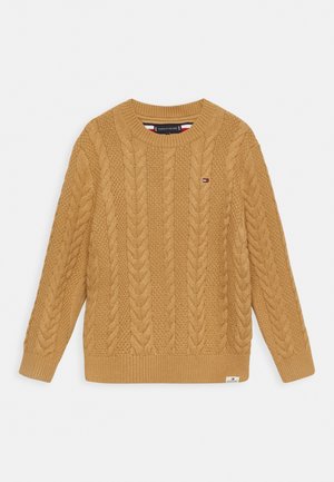 Musztardowożółty sweter w splot warkoczowy z długimi rękawami, okrągłym dekoltem i prążkowanym dołem. Na przodzie znajduje się mała naszywka z logo.