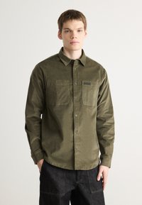 Olive green corduroy shirt with a button-down collar, two chest pockets, and a logo on the pocket. Textured fabric with a relaxed fit.