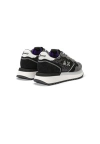 Zapatillas deportivas en ante negro y gris con un acabado texturizado. Presentan acentos blancos, forro morado y una suela de goma con un patrón en zigzag.