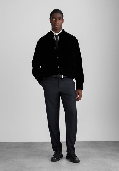 Black velvet button-up jacket with a pocket, paired with gray trousers and black lace-up shoes. Simple design, smooth texture.