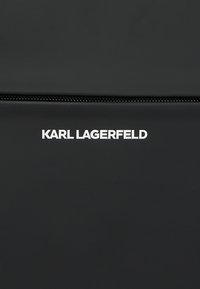 Czarna torba o gładkiej fakturze i górnym zamku błyskawicznym. Logo "KARL LAGERFELD" w białym kolorze wyraźnie widoczne z przodu.