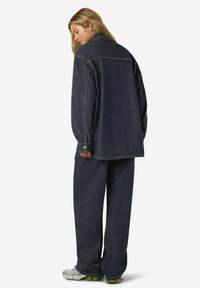 Temno denim obleka s preveliko jakno s ravnim krojem in širokimi hlačnicami. Nežne šive in kontrasti gumbov.