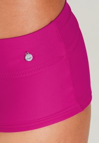 Fuchsia-Badehosen aus glattem Material mit einem silbernen Logopunkt und dekorativer Naht entlang des Bundes für einen zusätzlichen Akzent.