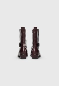 Bottines en cuir bordeaux au design épuré, avec fermeture éclair et détail de boucle sur le côté. Talon empilé pour plus de stabilité.